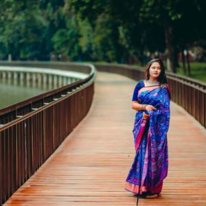 A woman in traditional sari strolls along a scenic wooden path in a lush park in Dhaka, Bangladesh.